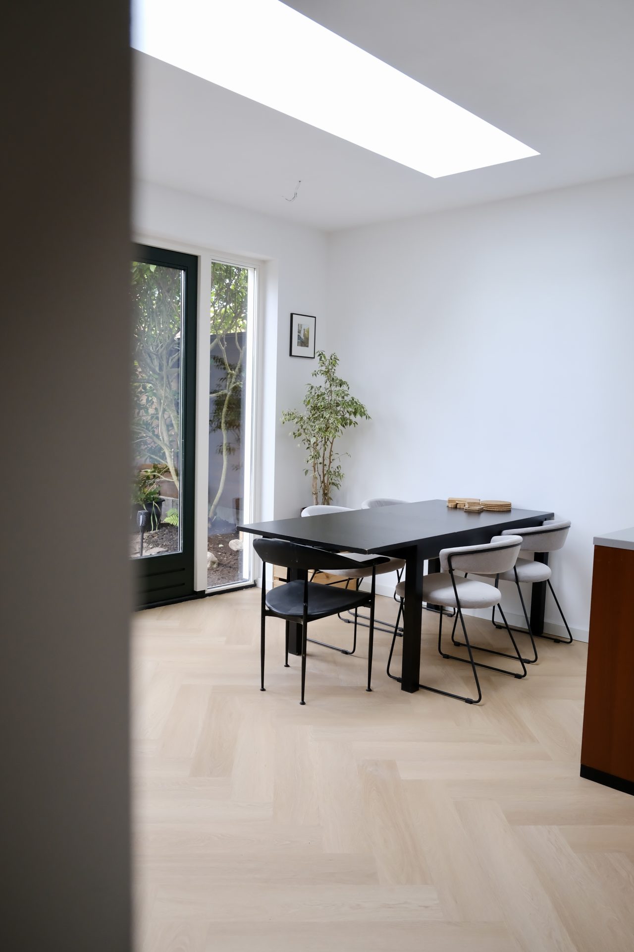 Lichte eetkamer met donkere eettafel, stoelen en grote glaspartij met uitzicht op groen