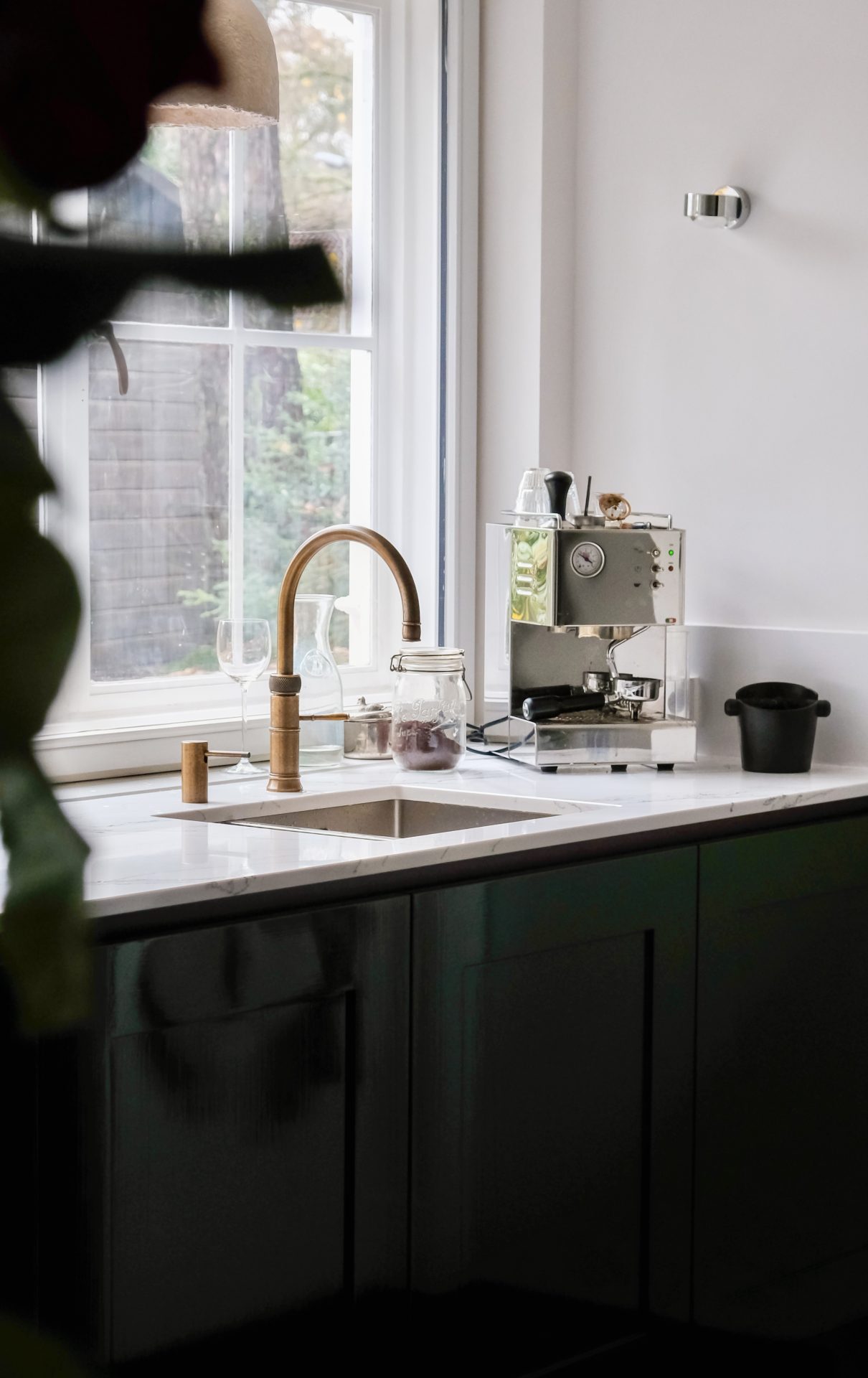 Moderne keuken met donkere onderkastjes, marmeren aanrechtblad en roestvrijstalen kraan, verlicht door natuurlijk daglicht