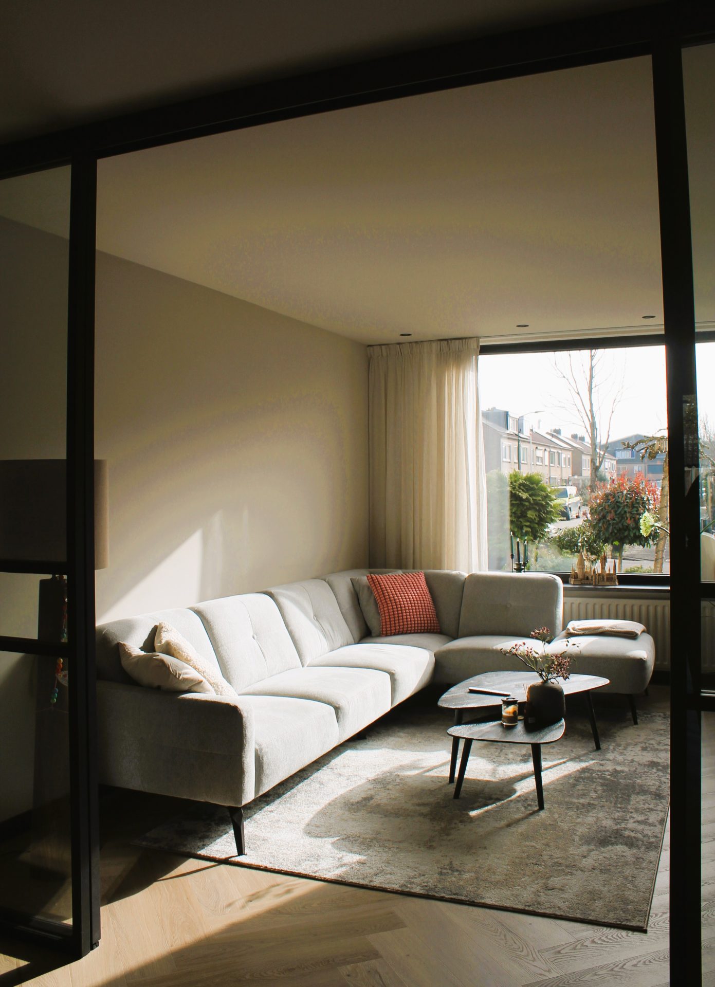 Lichte woonkamer na renovatie in Spakenburg met beige bank, salontafel en groot raam met uitzicht op tuin