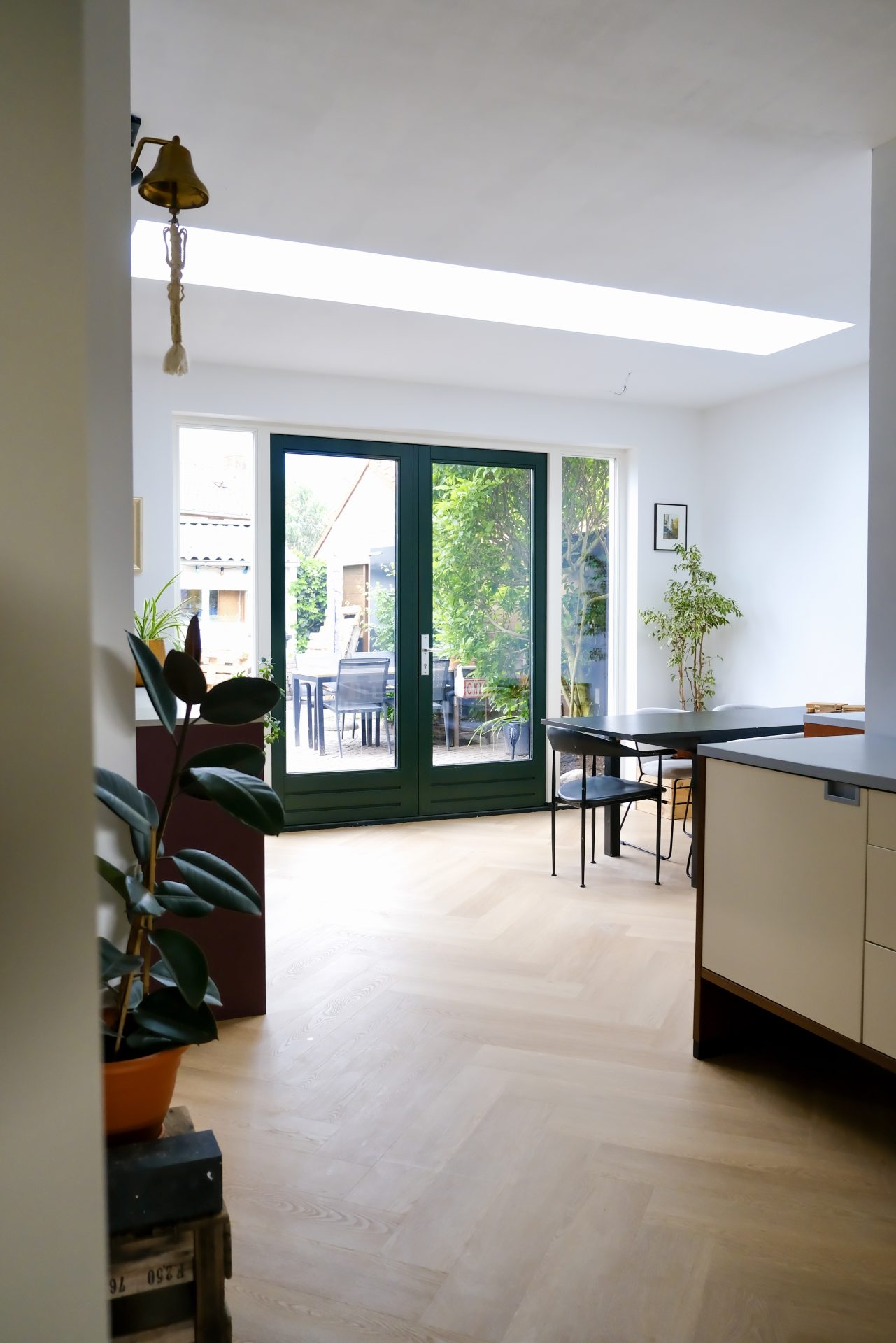 Lichte woon-keukenruimte met grote glazen tuindeuren, lichte vloer en doorkijk naar groene tuin