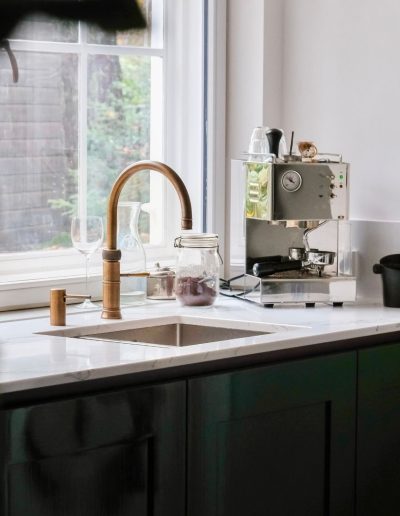 Moderne keuken met donkere onderkastjes, marmeren aanrechtblad en roestvrijstalen kraan, verlicht door natuurlijk daglicht