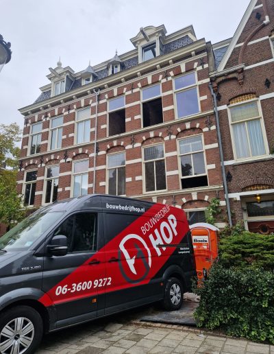 Vooraanzicht van een monumentaal bakstenen herenpand uit de negentiende eeuw met openslaande raamopening op de eerste verdieping, geparkeerde bedrijfswagen van Bouwbedrijf Hop op de voorgrond