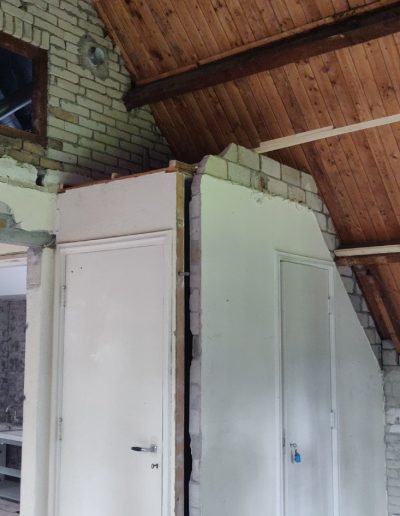 Ruimte in renovatie met zichtbare houten dakconstructie, metselwerk en twee witte deuren in ruwbouw