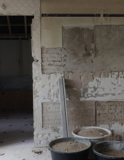 Ruimte in verbouwing met gestripte muren, zichtbaar metselwerk, leidingen en mortelbakken op de vloer