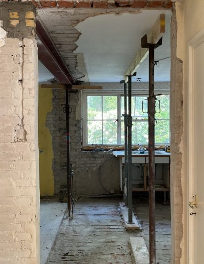 Doorbrekende muur tijdens renovatie met staalstempels als tijdelijke ondersteuning en zichtbaar metselwerk